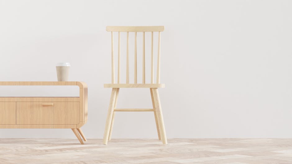 An interior scene during a home relocation process shows a light wooden chair with vertical slats on the backrest positioned near a minimalistic wooden sideboard with a white surface and a single drawer. On top of the sideboard sits a disposable coffee cup with a white lid. The setting features light-colored wooden flooring and a plain white wall in the background, indicating a clean, simplified environment. The scene appears to be in a doorway or loading area inside a house, with natural lighting illuminating the objects. The image captures the process of furniture handling and packing in the context of a house move, highlighting the careful arrangement of furniture and packing materials typical of professional removals by companies like Man With a Van Pimlico.